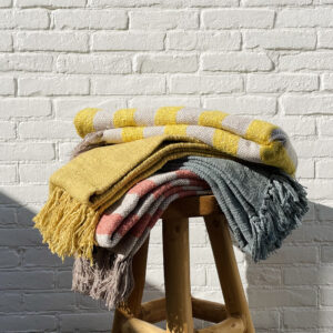 various throw blankets stacked on top of each other on a stool