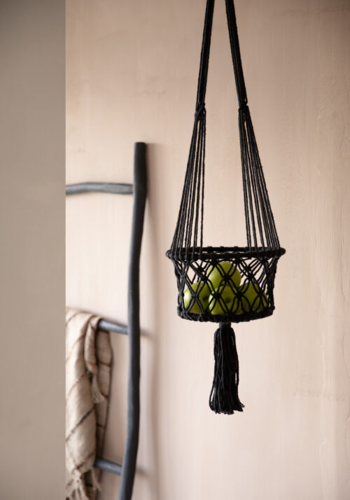 black macrame plant hanger with a black wooden rack with a blanket draped over it in the background
