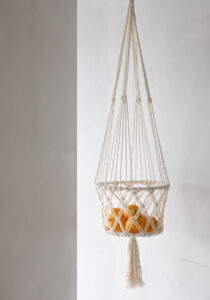 macrame white plant hanger filled with orange apples hanging in front of a white wall