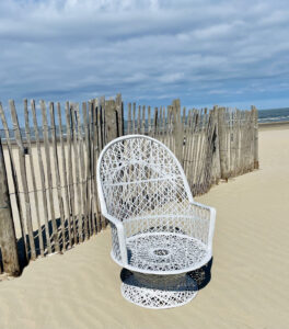 white woven chair on the beach in front of wooden posts