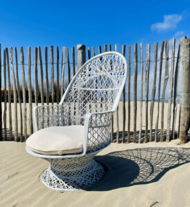 white braided chair on the beach in front of wooden fencing
