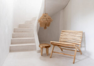 atmospheric photo of white concrete stairs with a teak table and lounge chair and hanging lamp made of seagrass