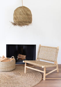 open haard met houten loungestoel, sisal tapijt, sisal lamp en rieten mand met houtblokken