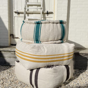 three poufs stacked on top of each other in the yard. All in the color broken white with stripes in green, gold and brown