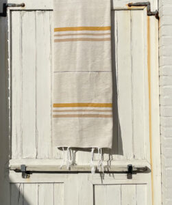 Pom pom deken in ecru met goudkleurige strepen hangend over een wiitte deur