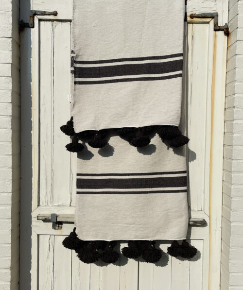 pompom deken, ecru met bruine ingeweven strepen hangend over een witte deur
