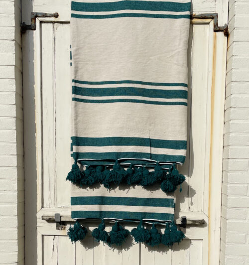 XXL Pom Pom blanket in off white with woven green emerald stripes hanging over an antique white door