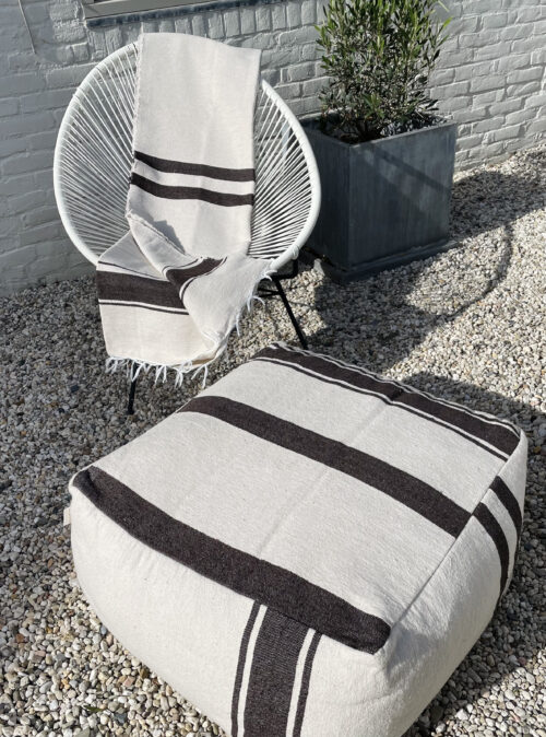 ecrukleurige poef en deken op een witte stoel in de tuin